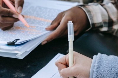 Foto ilustrativa: EBC Fotografia ilustrativa mostra as mãos de uma pessoa negra e de uma pessoa branca em close. Elas escrevem em papéis que se assemelham a provas ou relatórios.