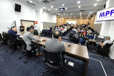 Fotos: MPF Foto mostra auditório com dezenas de pessoas nas cadeiras da plateia e três homens sentados por trás de bancada no palco. À direita, há um painel com a logo do MPF