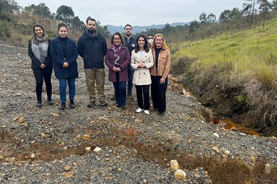 Foto: MPF Oito pessoas em pé posam para foto. Elas se encontram sobre um terreno pedregoso. À frente delas, se vê uma rachadura no solo, que se estende de um lado ao outro da imagem