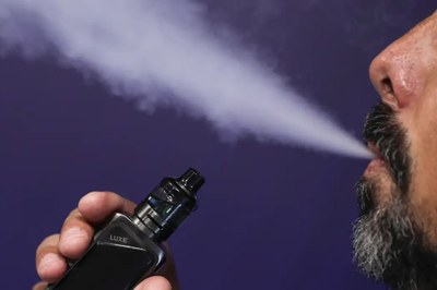Foto ilustrativa: Joédson Alves/Agência Brasil Homem com barba exala vapor pela boca enquanto segura um cigarro eletrônico preto, em frente a um fundo roxo.