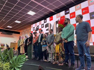 Foto: Seduc-MT autoridades indígenas e representantes de diversos órgãos posam em pé para foto em cima de um tablado