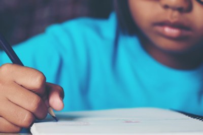 Imagem em detalhes de uma criança indígena escrevendo em um caderno com um lápis na mão