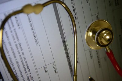 A imagem mostra um estetoscópio dourado sobre um formulário médico. 