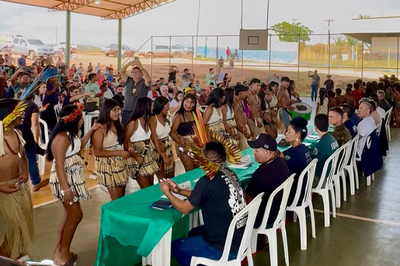 Foto mostra audiência pública realizada em quadra poliesportiva; indígenas estão em pé, em frente à mesa de autoridades