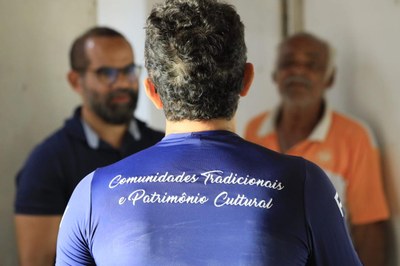 Equipe do MPF conversa com membro da comunidade. Da para ler, nas costas, a frase "Comunidades tradicionais e patrimônio cultural"