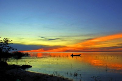 Foto: lubasi, sob licença CC BY-SA 2.0 Vista do lago ao entardecer, com o céu em tons de azul e laranja. No centro, um barco com uma pessoa.