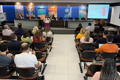 Fotos: Comunicação/MPF A imagem mostra uma reunião sendo realizada em um auditório. Uma mulher está em pé, falando ao microfone, diante de um público sentado.