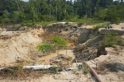 Área de garimpo em uma floresta, com uma grande cratera de terra e água barrenta em uma clareira desmatada.