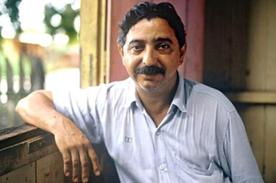 Foto mostra um homem de cabelo e bigode pretos, com camisa de mangas curtas azul clara, em casa de madeira e com o braço direito apoiado em janela