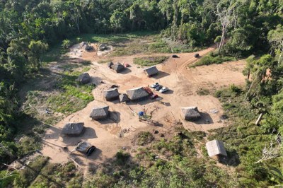 Foto: MPF Foto em vista aérea de uma pequena aldeia Parakanã em uma clareira na floresta. A aldeia possui cabanas com telhados de palha. Há veículos estacionados em um terreno de terra batida.