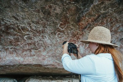Foto: Allerson Jesus Registro fotográfico de uma mulher fotografando inscrições circulares na pedra