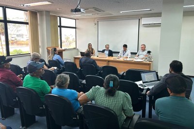 Fotografia de um auditório com pessoas sentadas na platéia e, ao fundo, a mesa das autoridades, com quatro homens e uma mulher.