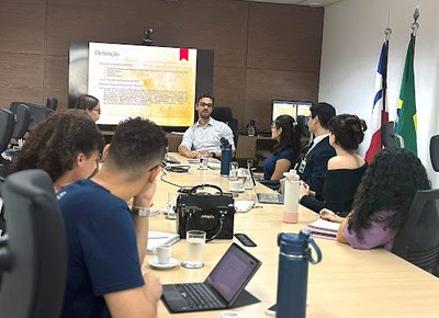 Encontro aconteceu na sede do MPF, em Salvador, Foto: Comunicação MPF/BA Foto de uma mesa com pessoas em volta, em uma reunião. Ao fundo uma tela de TV grande mostra uma apresentação em PowerPoint