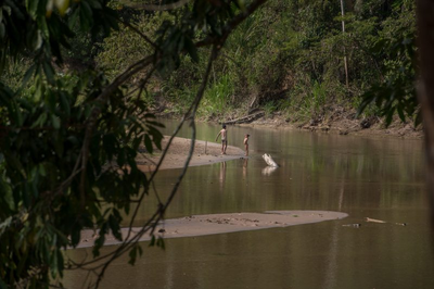Foto mostra duas crianças indígenas ao longe nas margens do Rio Gregório, com águas escuras e vegetação ao redor