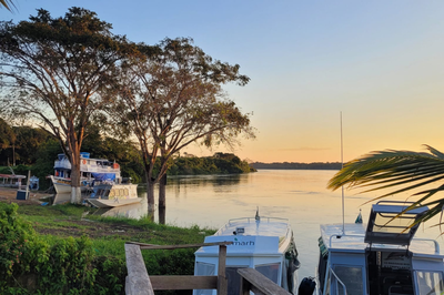 Foto mostra paisagem de margem de rio, com barcos de pequeno porte ancorados e vegetação 