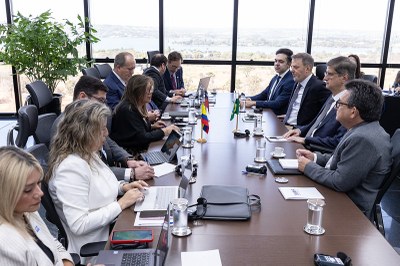 Foto: Antonio Augusto/MPF Foto mostra homens e mulheres vestidos formalmente sentados em torno de mesa comprida em sala de reunião. Alguns deles têm notebooks à frente, sobre a mesa, e há também pequenas bandeiras de países sobre a mesa