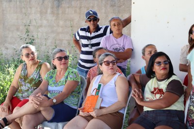 Foto com membros da comunidade sentados em cadeiras de plástico, olhando lateralmente para a direita, durante escuta ativa