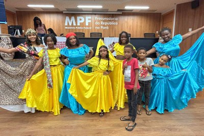 Crianças e mulheres em roupas de dança amarela e azul em um auditório com o fundo "MPF - Procuradoria da República no Pará".