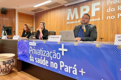 escuta-publica-privatizacao-saude-pa-2 Três pessoas sentadas em uma mesa em primeiro plano, com um painel azul na frente escrito "Escuta Pública - Privatização da saúde no Pará".