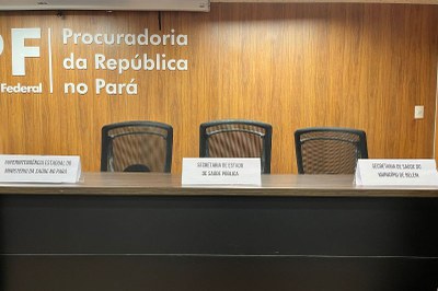 escuta-publica-privatizacao-saude-pa-3 Três cadeiras vazias atrás de uma mesa escura com placas de identificação: "Superintendência Estadual do Ministério da Saúde no Pará", "Secretaria de Estado de Saúde Pública" e "Secretaria de Saúde do Município de Belém".