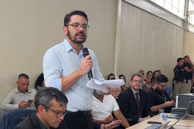 Audiência Residencial Girassol 2 O procurador regional dos Direitos do Cidadão no Pará, Sadi Machado, homem de óculos e barba, com camisa social azul clara, fala em um microfone enquanto segura papéis; pessoas o observam sentadas e em pé ao fundo