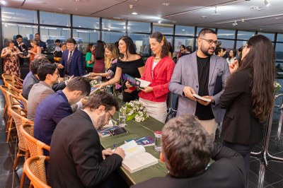 Foto: Leobark Rodrigues/ Comunicação MPF Pessoas se reúnem em uma mesa comprida. Em primeiro plano, um homem autografa um livro, enquanto outros interagem ao redor, com alguns segurando exemplares.