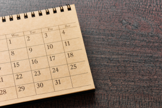 imagem de um calendário de mesa aberto, mostrando o mês com os dias organizados em colunas sobre uma superfície de madeira escura.
