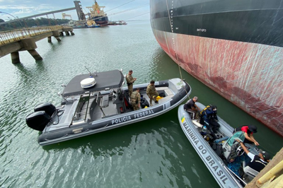 Foto: Polícia Federal Agentes da Polícia Federal e da Marinha do Brasil em botes de patrulha ao lado de um navio de carga atracado em um porto.