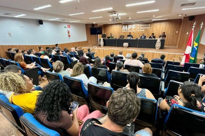 Foto: Comunicação MPF Auditório cheio com diversas pessoas sentadas em poltronas azuis, voltadas para uma mesa no palco com palestrantes e ao fundo o logotipo do MPF.