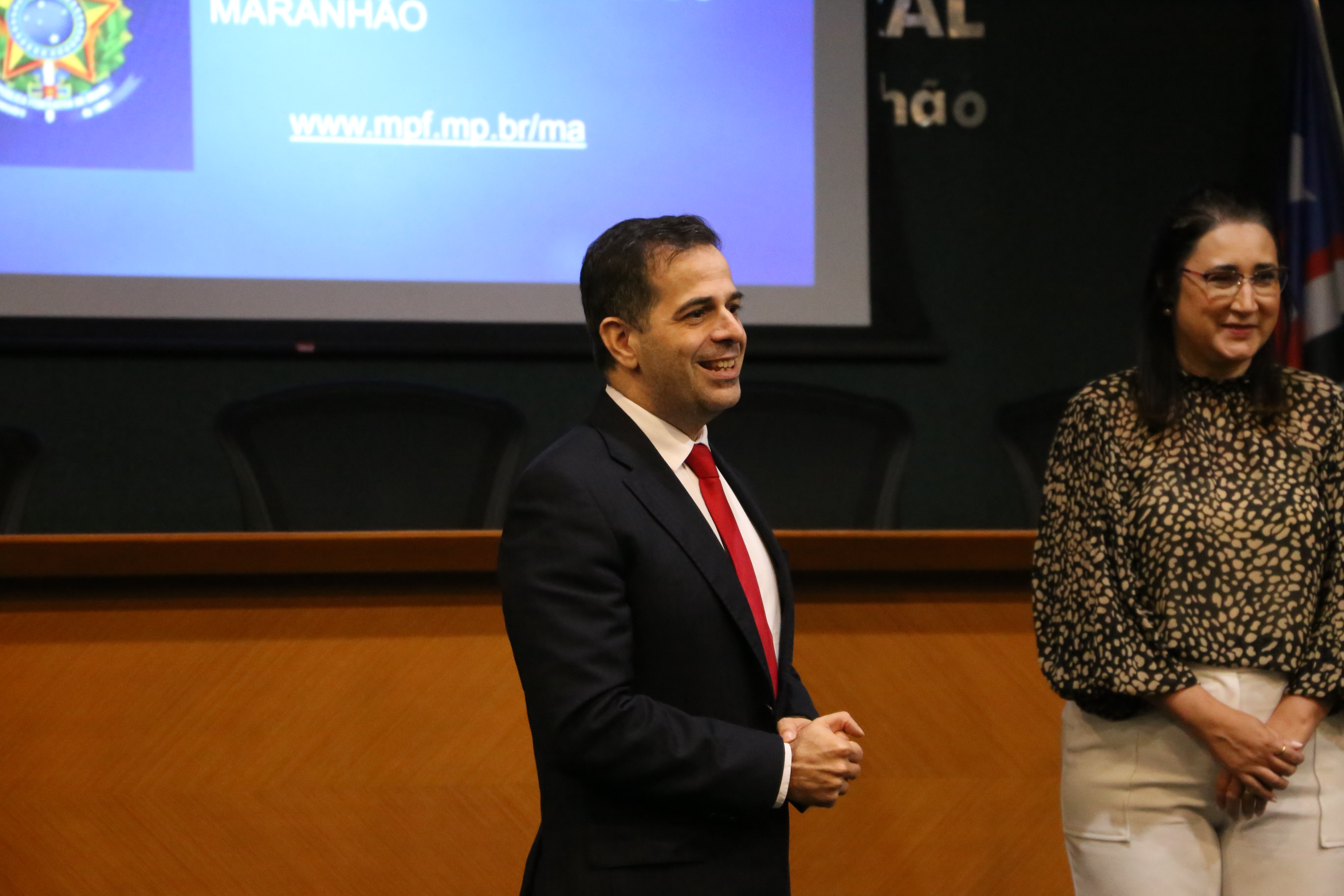 Procurador-chefe da Procuradoria da República no Maranhão aparece rindo em palestra, logo ao fundo podemos ver a coordenadora do curso de direito da Ufma.