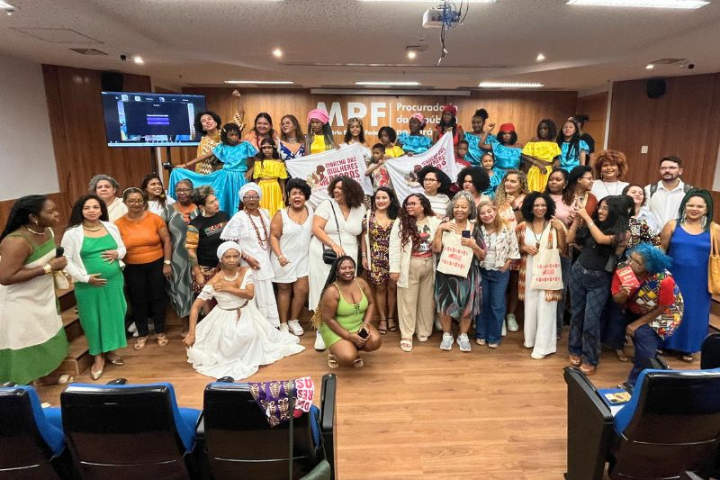 Cerca de quarenta pessoas, em sua maioria mulheres negras, posam em auditório com uma faixa da "Marcha das Mulheres Negras" no centro.