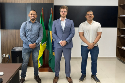 Foto: MPF/AP Três homens em pé, alinhados em uma sala de escritório, vestindo trajes sociais e casuais. Ao centro, entre eles, estão mastros com as bandeiras do Brasil e do Amapá.