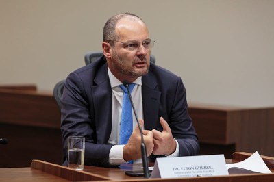 Foto: Leobark Rodrigues/MPF Fotografia de evento do novo corregedor. Ele está de terno, sentado à mesa com um microfone falando. Há um prisma com o nome à frente.