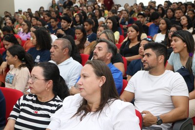 Imagens: Ascom MPF/BA Auditório cheio com dezenas de pessoas sentadas em cadeiras vermelhas, acompanhando atentamente um evento. Em primeiro plano, homens e mulheres de diferentes idades estão voltados para a frente, enquanto ao fundo vê-se uma plateia diversa e concentrada.