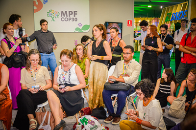 Fotos: Vam Gonçalves/MPF Foto de uma mulher em pé falando em um microfone para uma plateia sentada e em pé em uma reunião no evento MPF COP30.