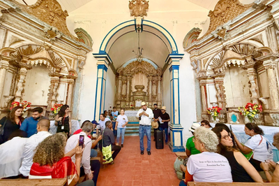 foto mostra interior da capela, com várias pessoas sentadas, durante ato 