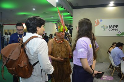 Foto de indígena em pé conversando com duas pessoas no estande do MPF na COP30