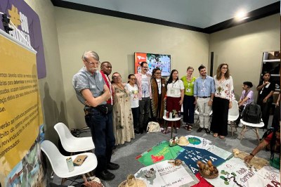Foto da roda de conversa, com cartazes e bandeiras das comunidades tradicionais no chão, e pessoas em pé em volta
