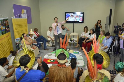 Foto mostra roda de conversa com indígenas e povos tracionais sentados em círculo; ao centro o procurador em pé enquanto fala; ao centro, no chão, cartazes e bandeiras da comunidades
