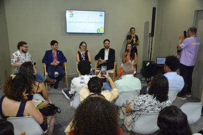 Fotos: Vam Gonçalves/MPF Foto mostra painel de debate sobre "Legal remedies for climate disasters" com cinco participantes sentados em cadeiras e uma debatedora falando ao microfone para uma plateia.