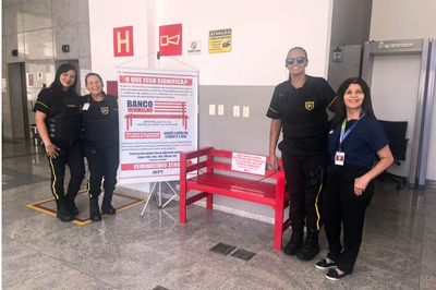 Quatro mulheres, incluindo duas em uniformes de segurança, posando ao lado de um Banco Vermelho e um banner do MPF sobre a luta contra a violência de gênero (Feminicídio Zero).