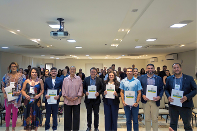 Foto de nove pessoas (participantes ou palestrantes) segurando certificados do Governo do Acre em um evento.