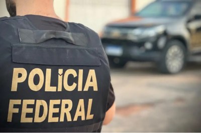 Foto: Polícia Federal/ Divulgação Imagem mostra agente da Polícia Federal de costas, com colete onde se lê o nome da instituição. Ao fundo, uma viatura da PF desfocada