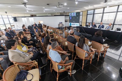 Foto: Leobark Rodrigues/Secom/MPF A foto mostra um espaço de eventos com o público sentado em cadeiras e, em frente, uma mesa composta por uma mulher e três homens fazendo uma apresentação.