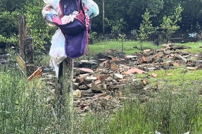 Foto: Comunicação MPF Foto colorida mostra, em primeiro plano, uma mochila meio aberta e sacolas penduradas em um poste de madeira rústico à esquerda. O poste está numa área com vegetação alta e verde. Atrás da mochila, há um monte de entulho composto por pedaços de tijolos vermelhos e destroços de construção espalhados sobre o solo. Ao fundo, há mais vegetação e algumas árvores pequenas. O dia está nublado.