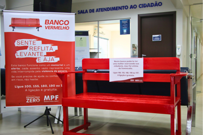 Foto de um banco vermelho mostrando a frase: Neste banco poderia ter uma mulher exercendo sua cidadania, mas foi vítima de feminicídio. Disque 100, 180, 190, 197.