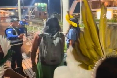 Foto noturna de um bloqueio com pessoas indígenas em primeiro plano e, ao fundo, um segurança de colete e grades de metal.