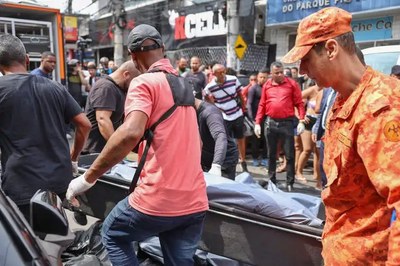 Foto mostra Bombeiros e civis carregando macas com corpos 
