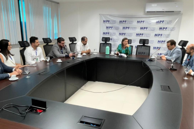 A imagem mostra uma reunião realizada em uma sala de conferências da Procuradoria da República em Alagoas (MPF/AL). Os participantes estão sentados em torno de uma grande mesa em formato de “U”, com notebooks, copos e xícaras à frente.

Ao fundo, há um painel institucional do MPF, e a procuradora da República Niedja Kaspary aparece ao centro, conduzindo a conversa. Ela usa um vestido verde estampado e está acompanhada por representantes de diferentes instituições, que ouvem atentamente e participam da discussão.