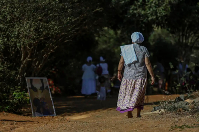 Foto: Marcelo Camargo/Agência Brasil Foto mostra uma mulher idosa com lenço branco na cabeça caminhando em estrada de terra em direção a um grupo de pessoas de roupas brancas, em uma comunidade tradicional ou quilombo.